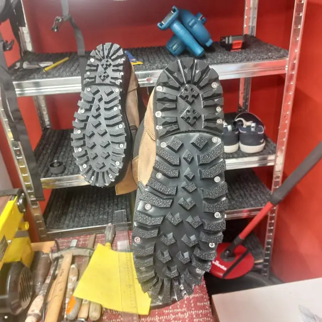 Detail pevné podrážky se šrouby na pracovní obuvi v dílně.