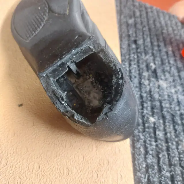 Detail poškozené patní části černé obuvi před opravou.
